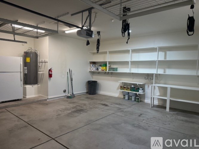 A large, empty room with a white fridge, a fire extinguisher, and some shelves with items on them.