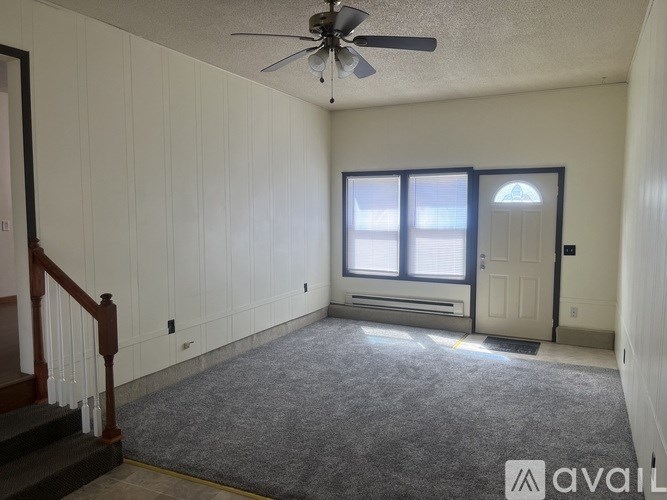 A room with a carpeted floor, a ceiling fan, and a door with a window.