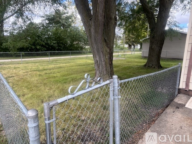 A chain link fence with a metal gate and a tree in the background.