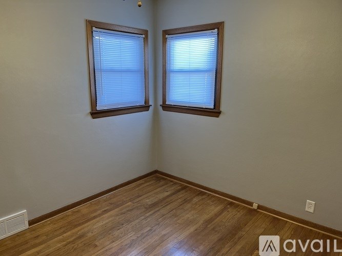 Two windows with blinds in a room with wooden floors.