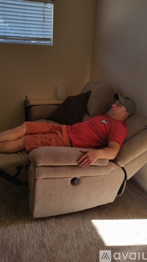 A man in a red shirt and khaki shorts is lying on a beige couch.