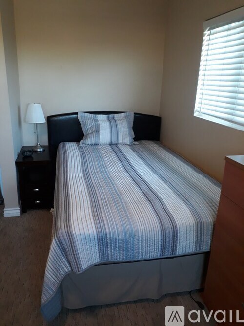 A bed with a striped comforter and two pillows sits in a room with a lamp and a window.