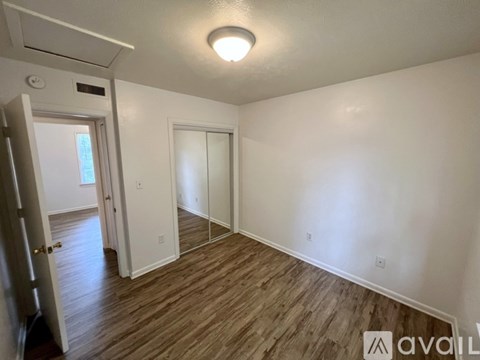 A room with wood flooring and white walls, with a door on the left and a window on the right.