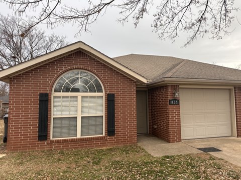 A brick house with a white garage door and a window with black shutters.