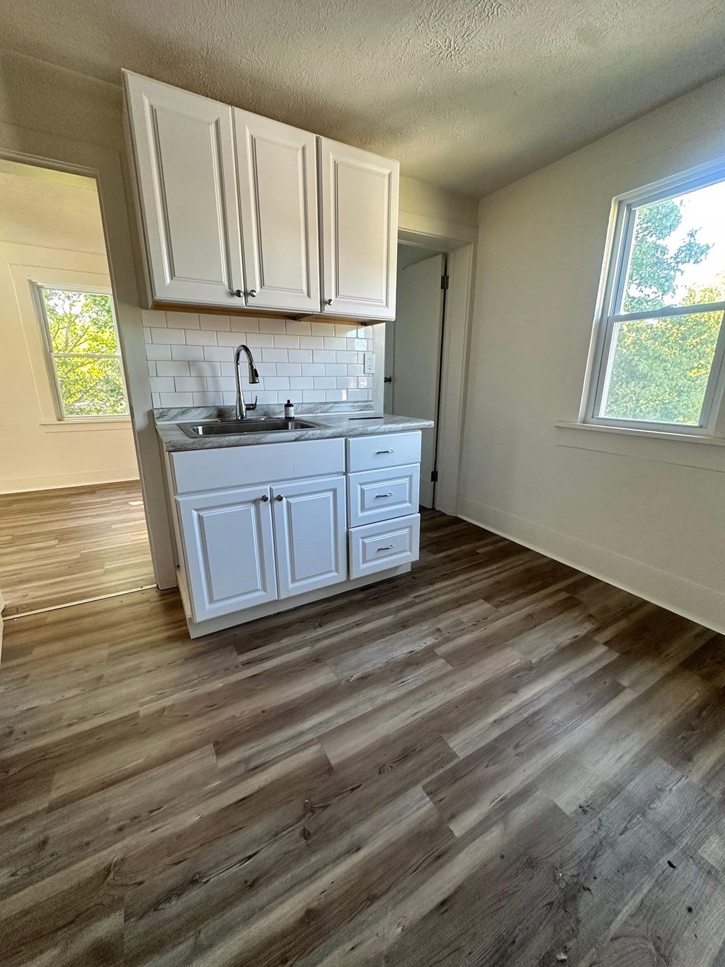 A kitchen with white cabinets and a wooden floor.