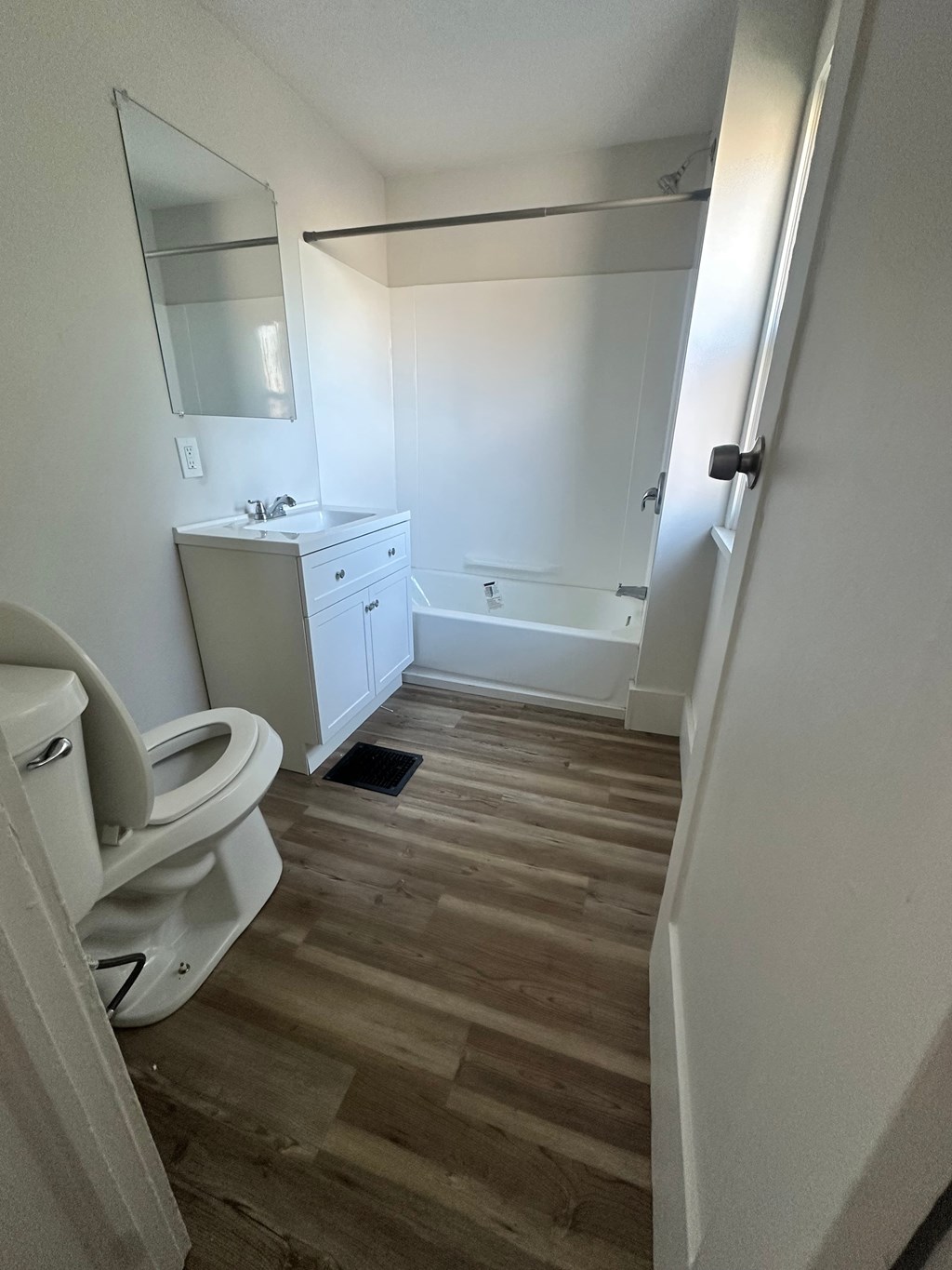 A white bathroom with wood flooring and a white toilet.