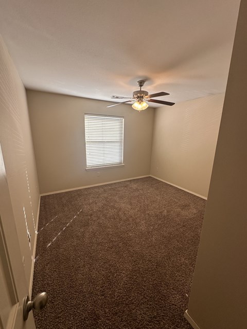 A room with a carpeted floor and a ceiling fan.