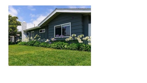 A house with a blue exterior and white trim is surrounded by a well-kept lawn and flowering plants.