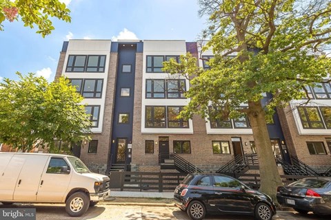 A white van is parked in front of a building with a tree in front of it.