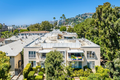A large house with a flat roof and a balcony is surrounded by trees.