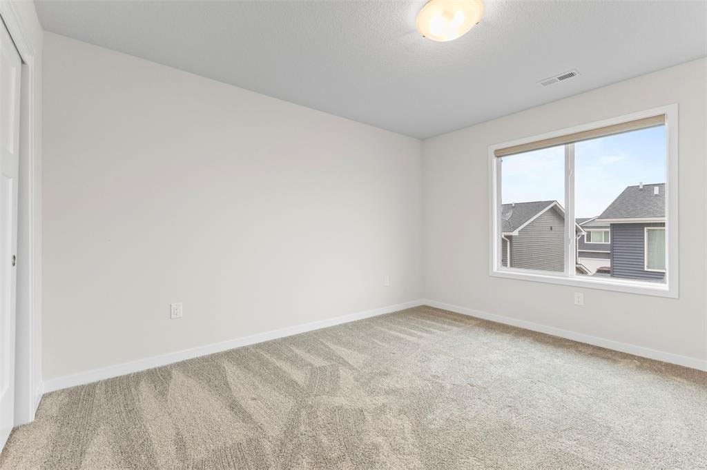 A room with a carpeted floor and a window showing a view of houses outside.