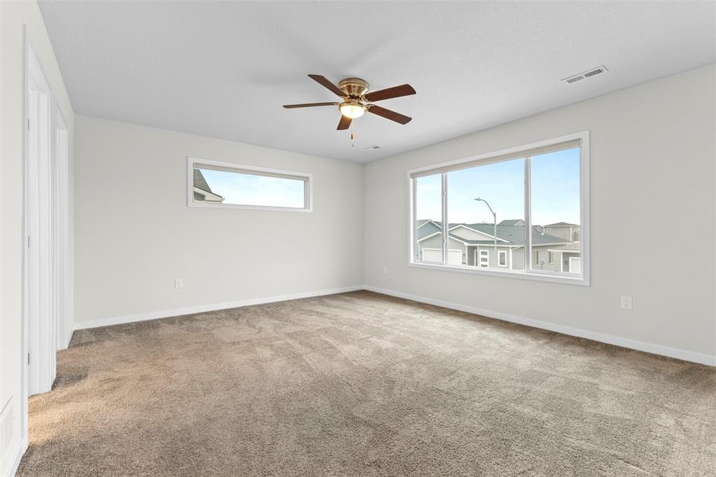 A room with a ceiling fan and a window showing a view of houses.