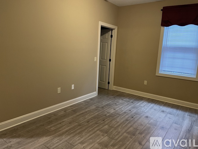 A room with a wooden floor and a door leading to another room.