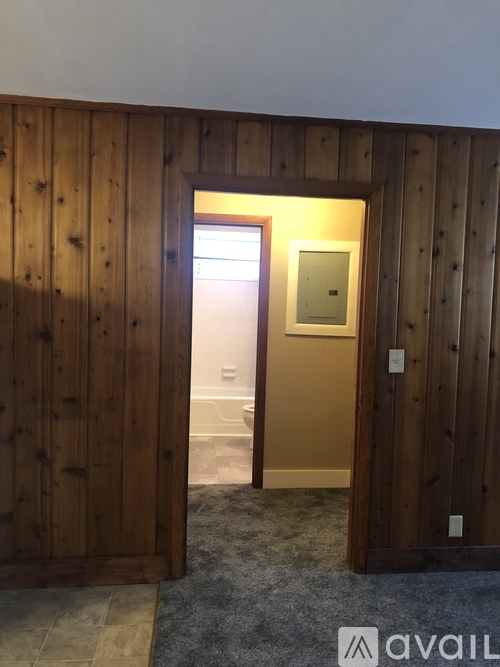 A room with wooden walls and a doorway leading to another room.