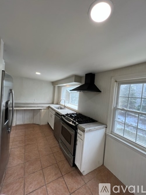 A kitchen with a black hood, white cabinets, and a tiled floor.