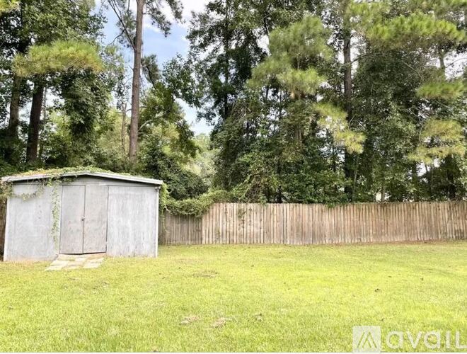 A shed sits in a grassy field with a wooden fence and trees in the background.