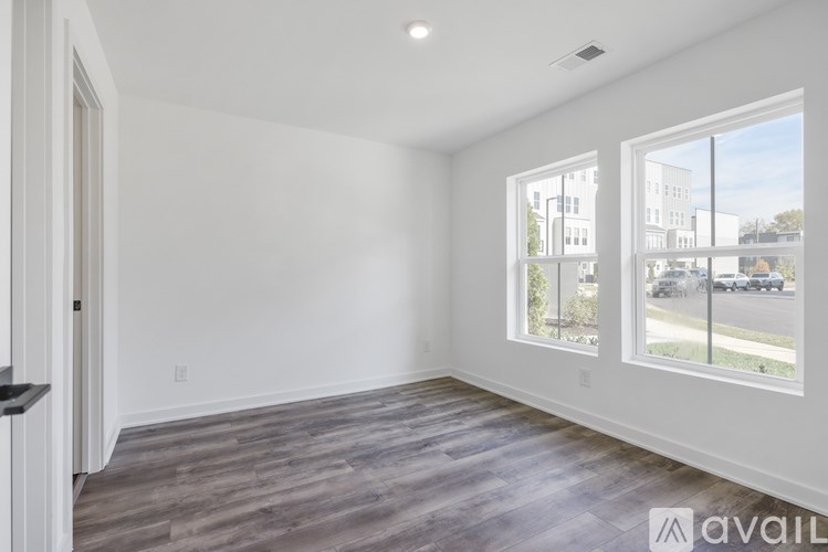 A spacious room with wooden flooring and large windows overlooking a street.