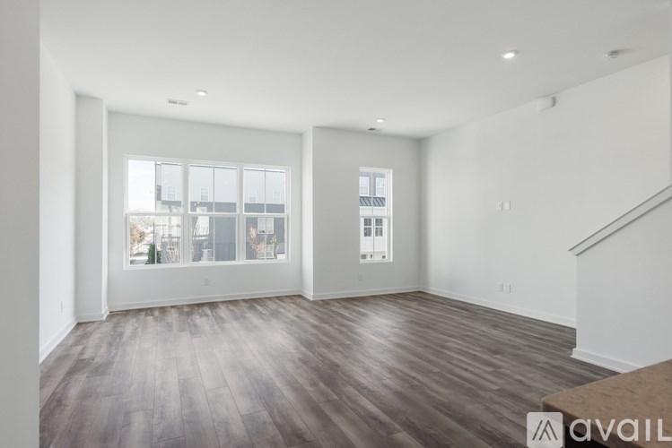 A spacious room with wooden floors and a staircase on the right side.