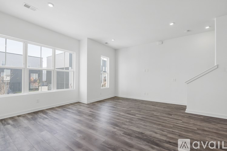 A spacious room with wooden flooring and a staircase on the right side.