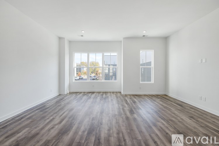 A spacious room with wooden flooring and two windows.