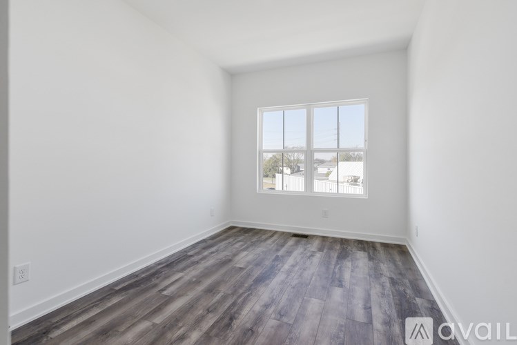 A room with a large window and wooden flooring is available for rent.