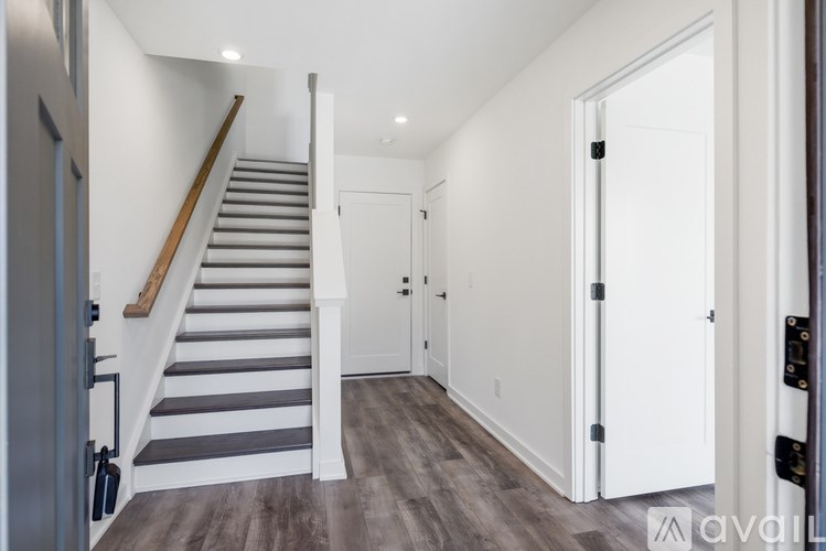A staircase with a wooden handrail and white steps leads to a white door.