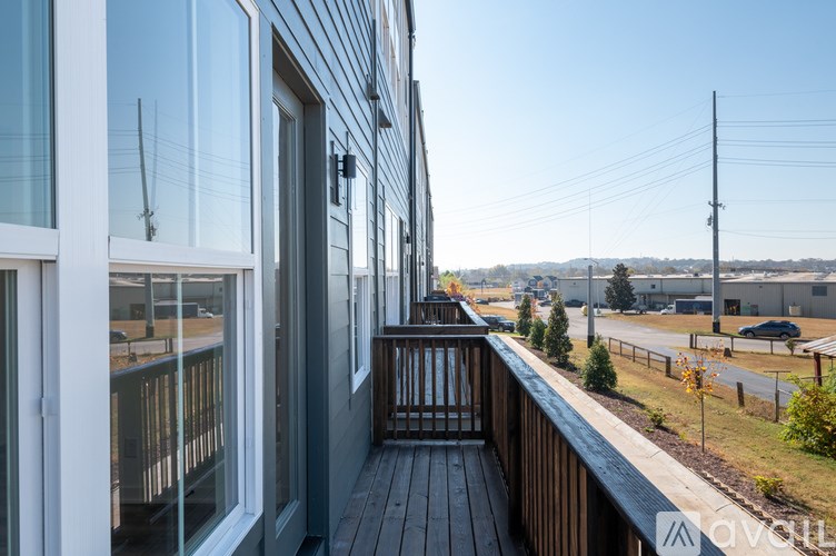 A balcony with a wooden railing and glass doors overlooks a parking lot and distant buildings.