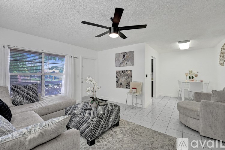 A living room with a grey couch, a striped pillow, a fan, and a white wall.