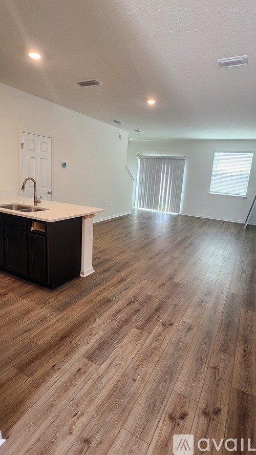 A room with wooden flooring and a kitchen area with a sink and cabinets.