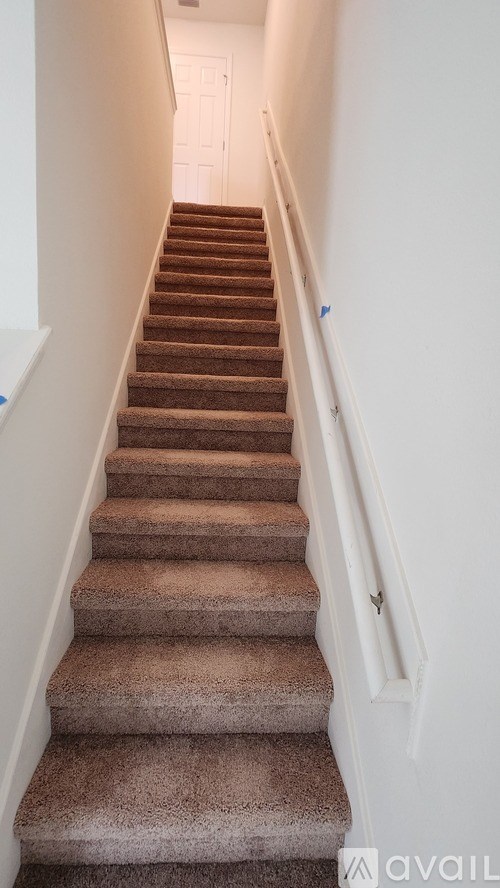 A staircase with a brown carpeted runner and white walls.