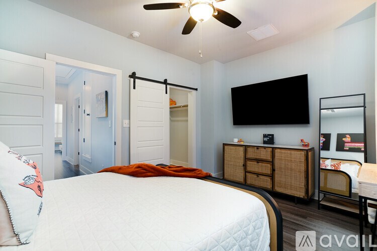 A bedroom with a bed, a ceiling fan, and a TV mounted on the wall.