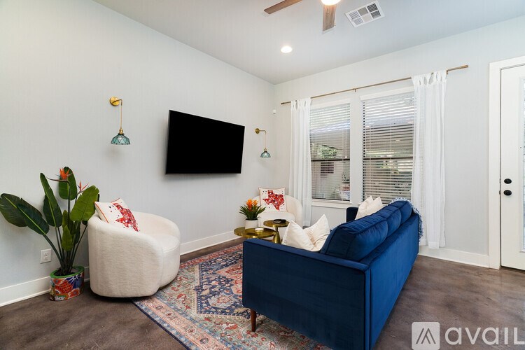 A living room with a blue couch, a white chair, and a flat screen TV mounted on the wall.