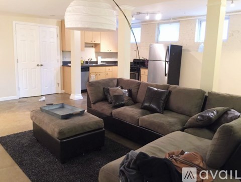 A living room with a couch, ottoman, and kitchen area in the background.