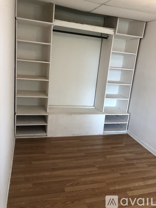 A room with a white wall and a wooden floor with a shelving unit.