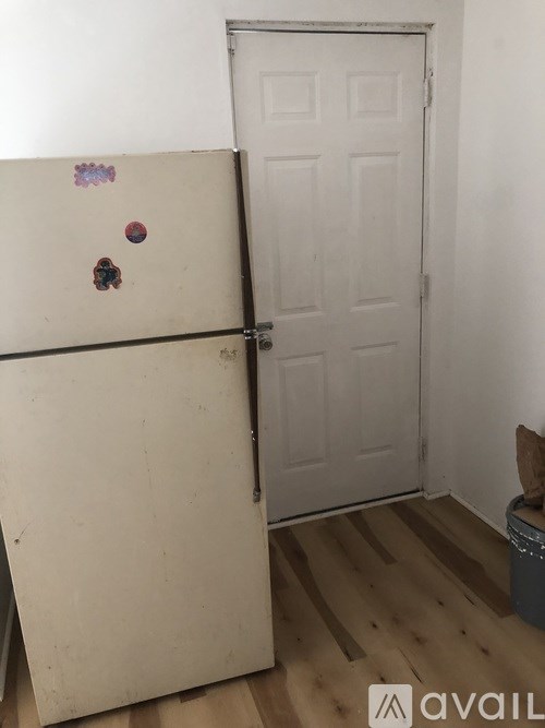 A white door is in a room with a white wall and a white fridge.