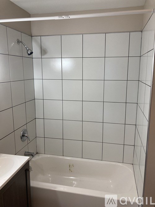 A white tiled shower area with a white bathtub and a white sink.
