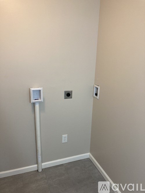 A white pipe with a box on top stands in a corner of a room.