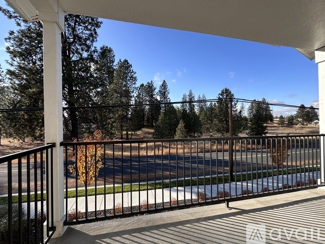 A balcony with a black railing overlooks a road and trees.