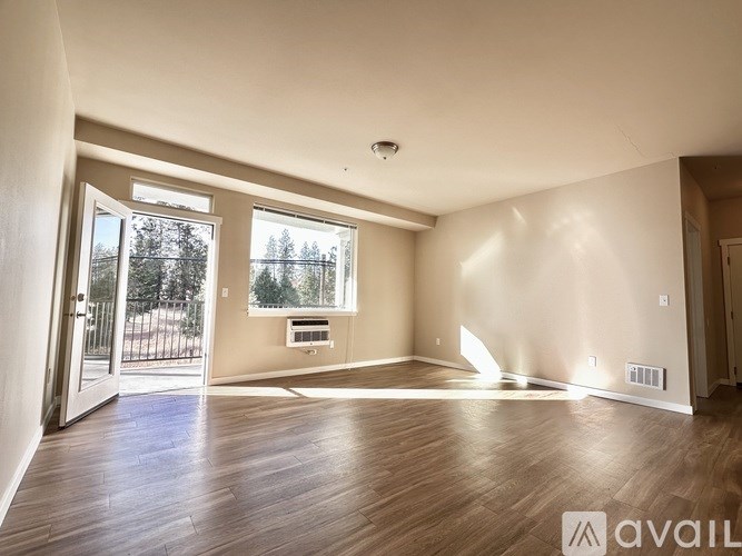 A spacious room with wooden floors and a large window overlooking a tree-filled landscape.