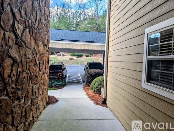 A stone wall next to a house with a window and a car parked in the driveway.