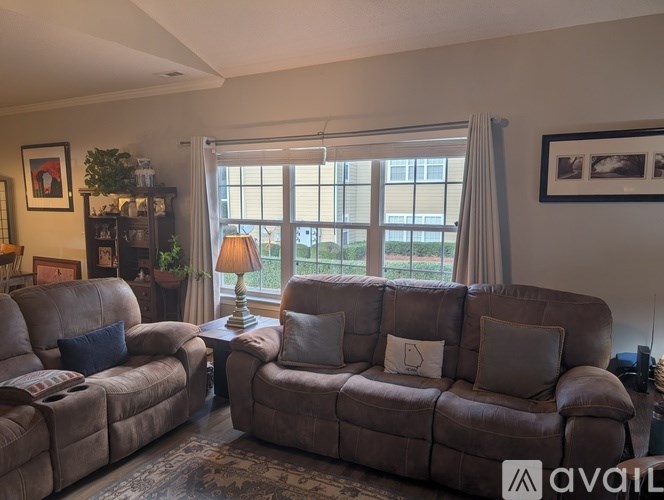A living room with a brown couch, a brown leather armchair, a brown leather sofa, a small table with a lamp, a potted plant, and a framed picture on the wall.