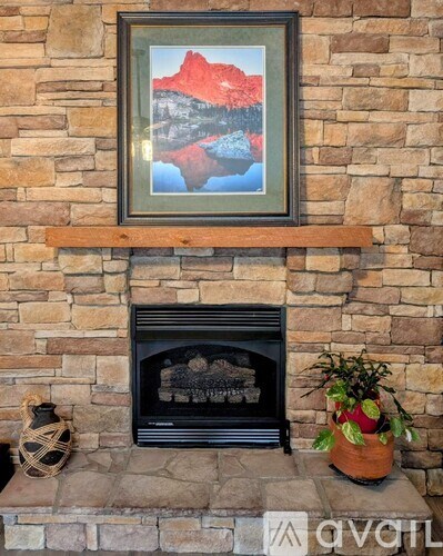 A framed picture of a mountain is hanging above a fireplace.