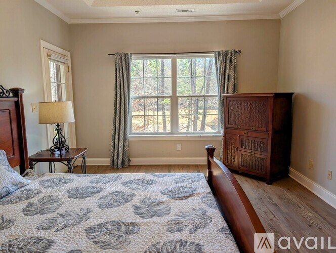 A bedroom with a large bed, a nightstand, and a window with a view of trees.