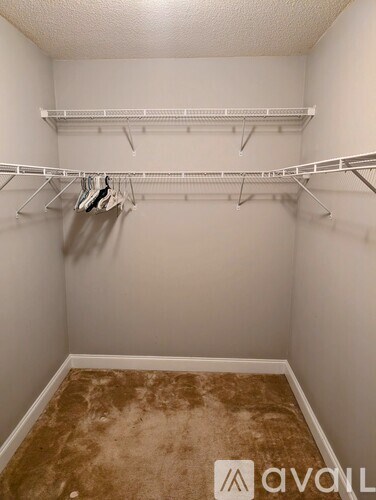 A room with a carpeted floor and a wall-mounted shelf with clothes hanging on it.
