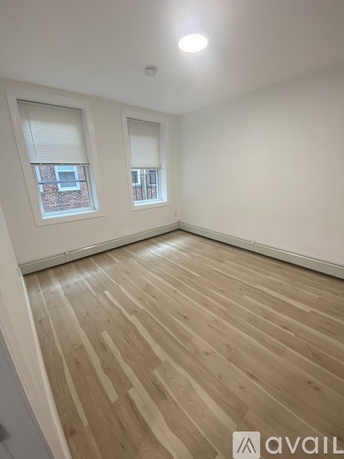 A room with wooden flooring and two windows.
