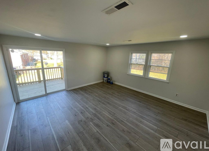 A spacious room with wooden flooring and a sliding glass door leading to a deck.