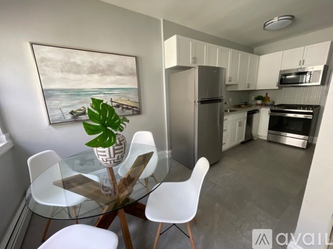 A kitchen with a glass table and chairs, a fridge, and a painting of a beach scene on the wall.