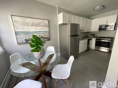 A kitchen with a glass table and chairs, a fridge, and a painting of a beach scene on the wall.