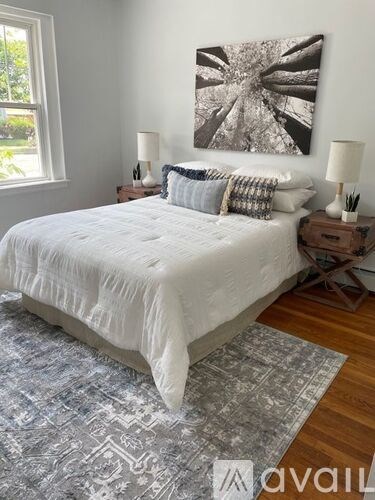 A bed with a white comforter and a grey and white patterned rug in front of it.
