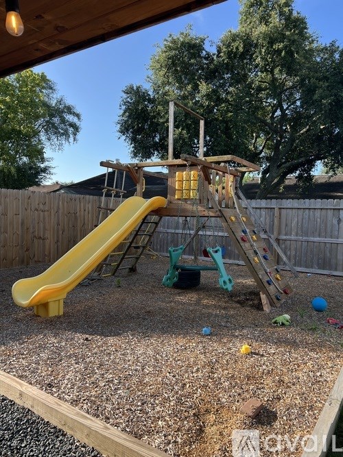 A yellow slide in a playground with a wooden structure.
